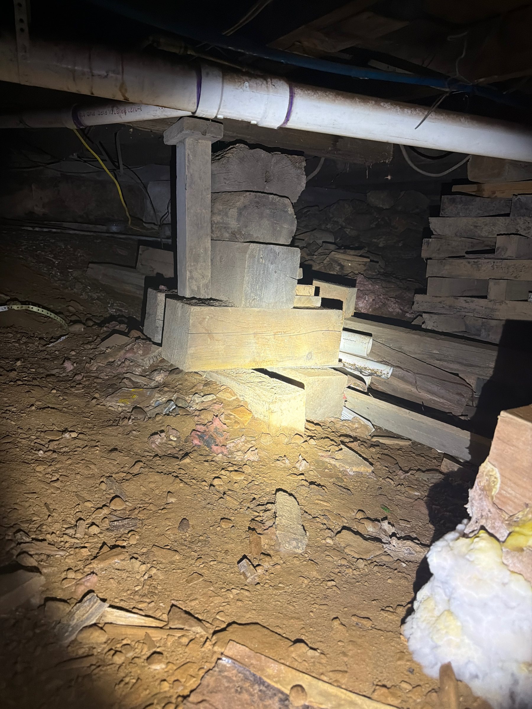 Improvised wood and stone support beneath floor framing in a crawlspace